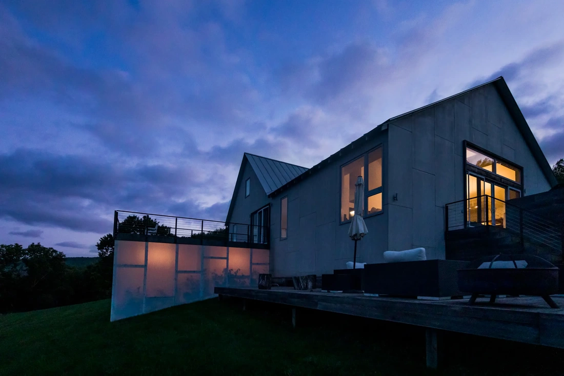 Luxury Catskills vacation rental called The Roxbury Estate glowing at dusk with lights on.